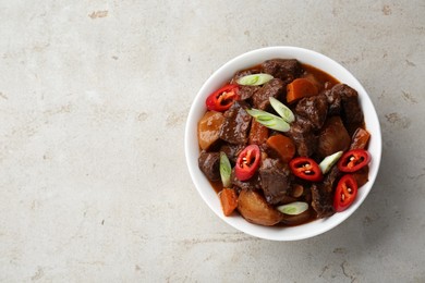 Delicious beef stew with carrots, chili peppers, green onions and potatoes on white textured table, top view. Space for text