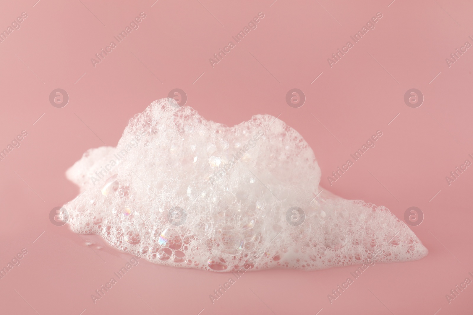 Photo of Fluffy bath foam on pink background, closeup. Care product