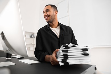 Photo of Happy man with documents at grey table in office, low angle view