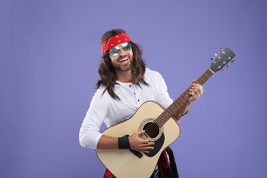 Photo of Stylish hippie man in sunglasses playing guitar on violet background