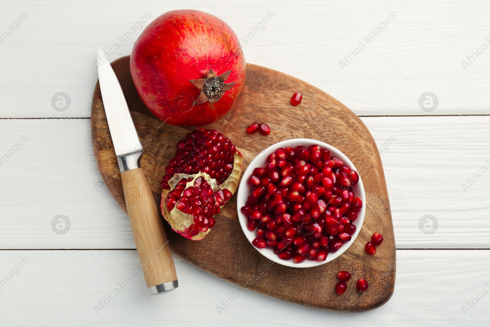 Photo of Ripe juicy pomegranate with grains and knife on white wooden table, top view