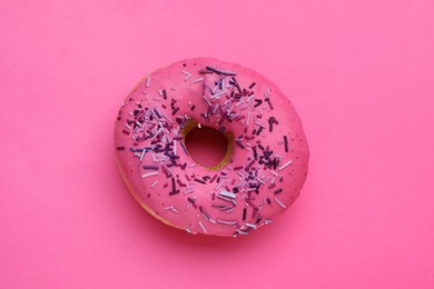 Photo of Sweet glazed donut decorated with sprinkles on pink background, top view. Tasty confectionery