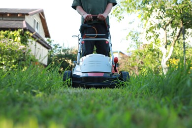 Photo of Man cutting grass with lawn mower in garden, closeup