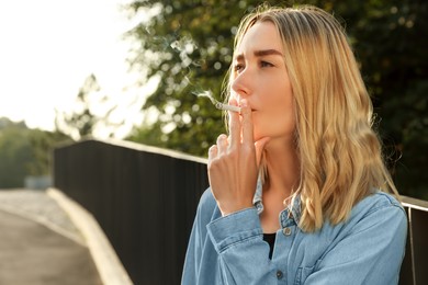 Photo of Young woman smoking cigarette outdoors, space for text