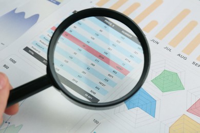 Accountant looking at document through magnifying glass, closeup