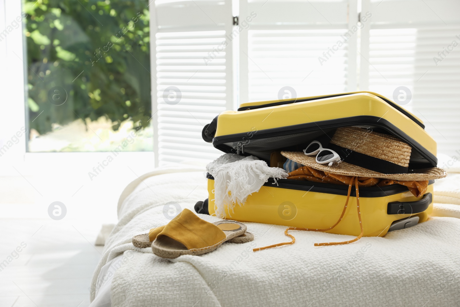 Photo of Open suitcase full of clothes, shoes and summer accessories on bed in room