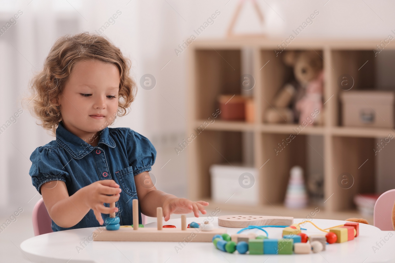 Photo of Motor skills development. Little girl playing with stacking and counting game at table indoors