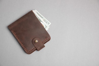 Stylish brown leather wallet with dollar banknotes on light grey background, top view. Space for text