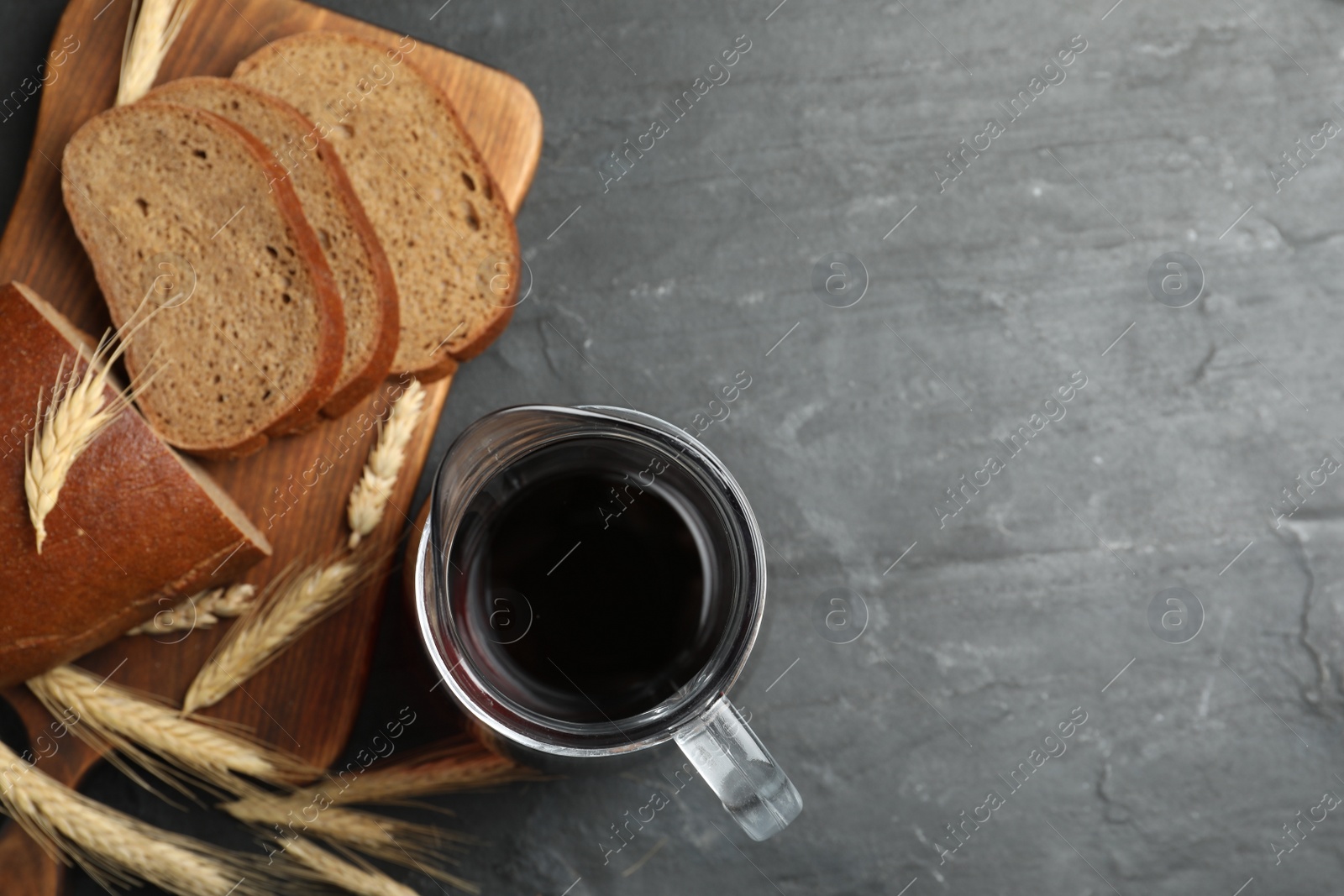 Photo of Delicious kvass, bread and spikes on black slate table, flat lay. Space for text