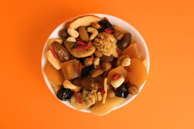 Bowl with mixed dried fruits and nuts on orange background, top view