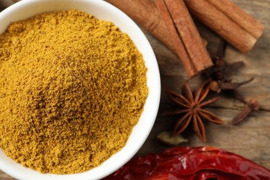 Dry curry powder in bowl and other spices on wooden table, flat lay