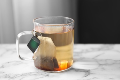 Photo of Tea bag in cup of hot water on white marble table