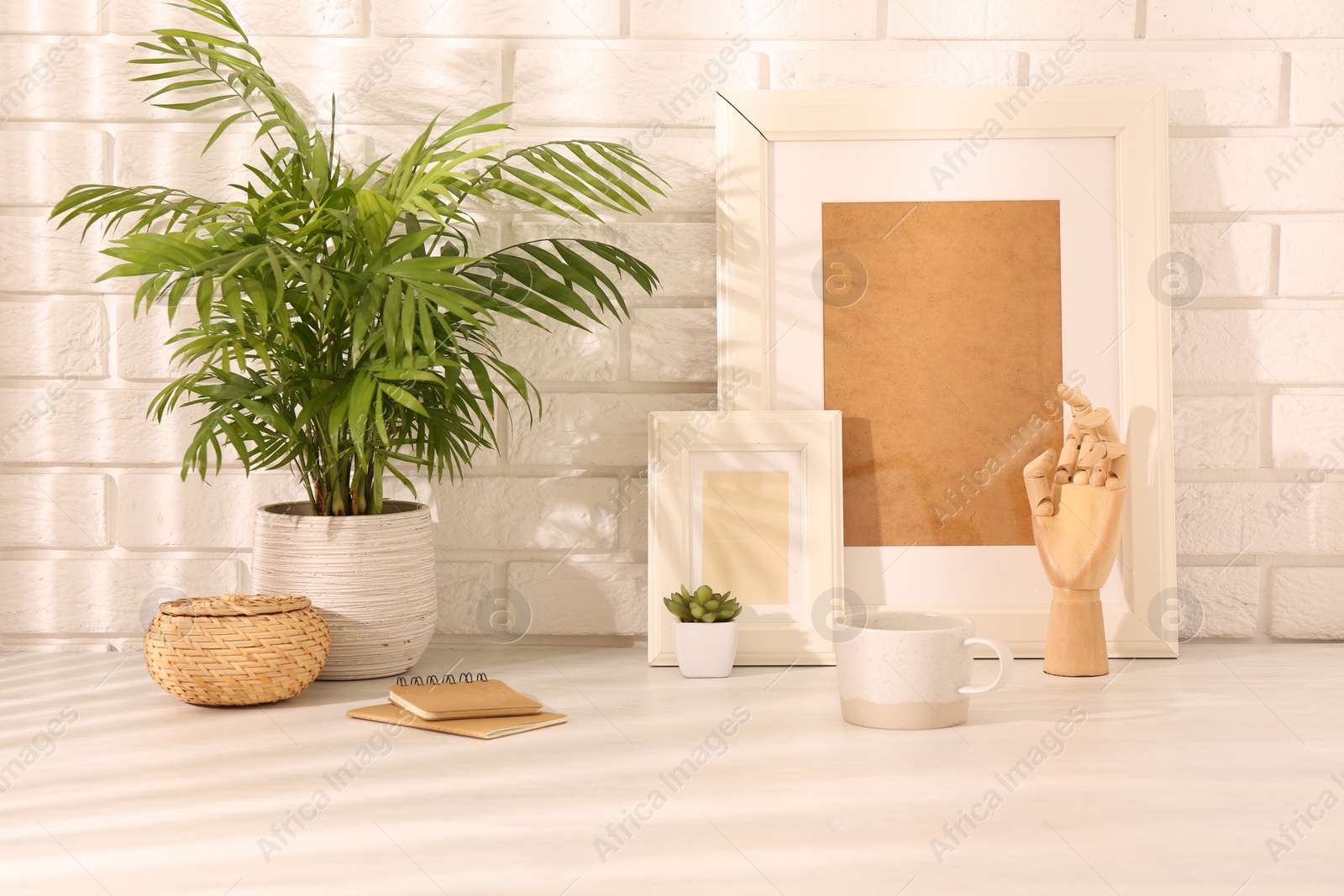 Photo of Stylish office workplace. Decor elements, plants, cup and notebooks on white table near brick wall