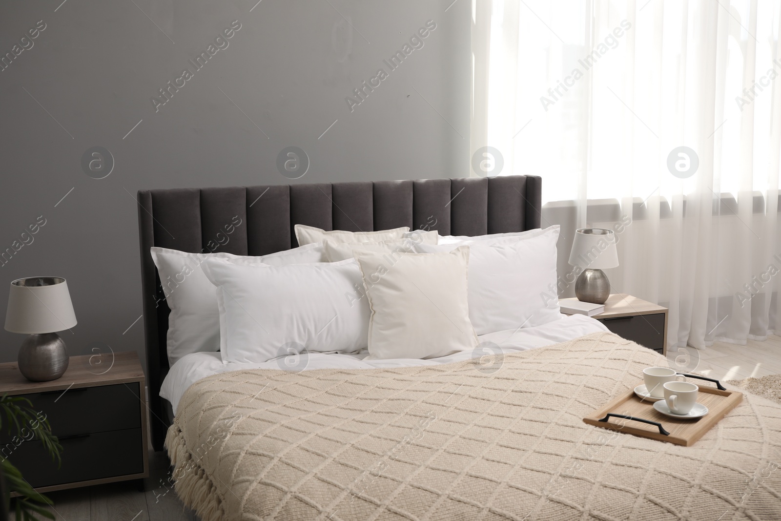 Photo of Many soft white pillows and knitted blanket on bed indoors