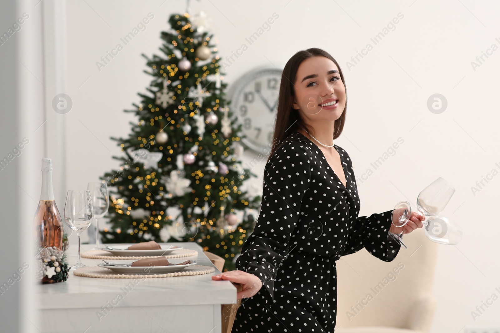 Photo of Christmas mood. Smiling woman holding empty glasses near dining table indoors