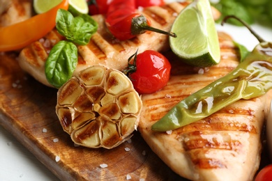 Tasty grilled chicken fillets with vegetables and lime on wooden board, closeup