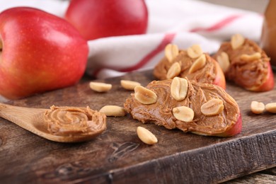 Photo of Pieces of fresh apple with peanut butter on wooden board, closeup