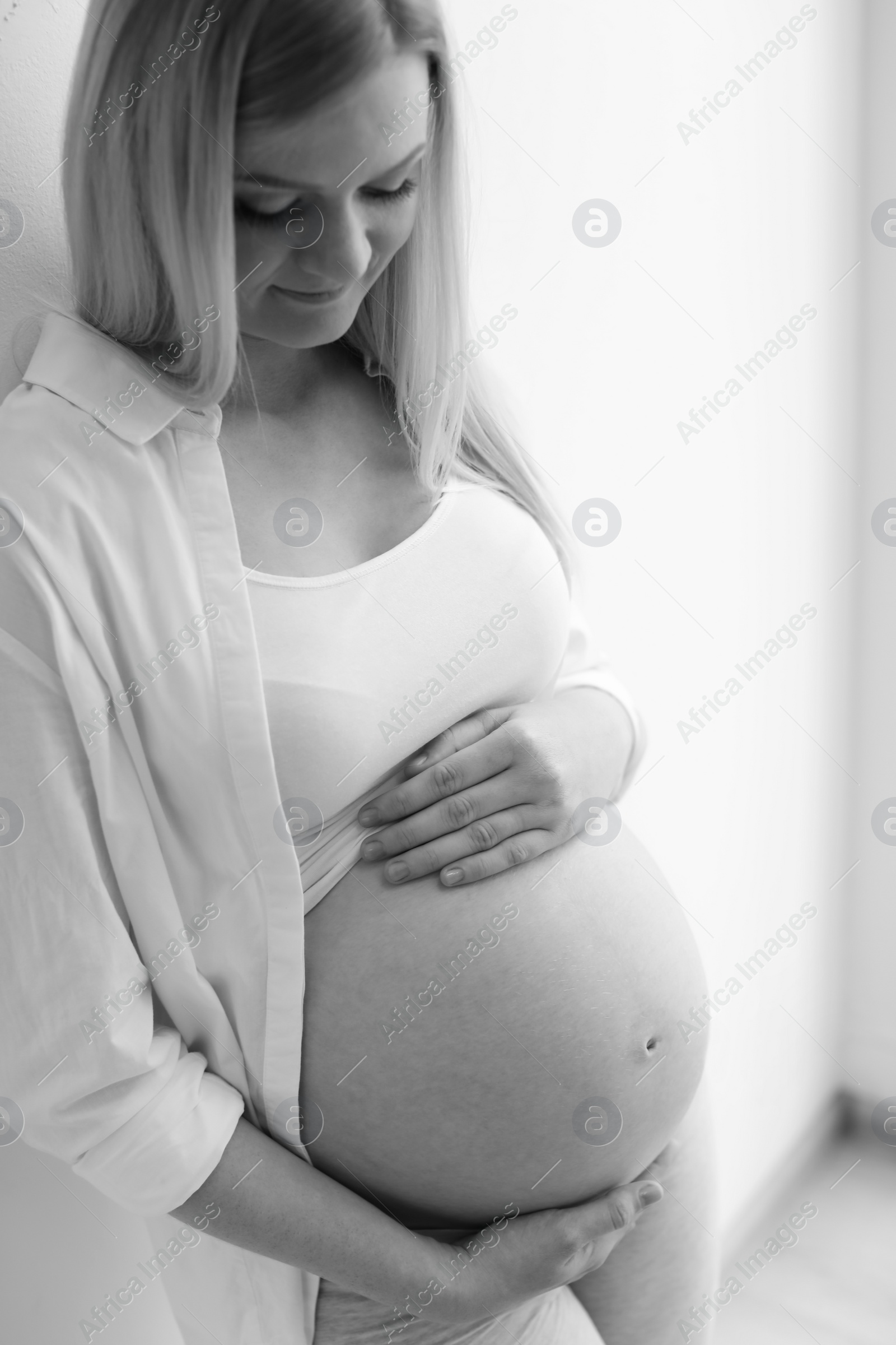 Photo of Pregnant woman near light wall, black and white effect