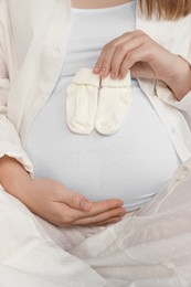 Photo of Pregnant woman with baby socks on bed, closeup