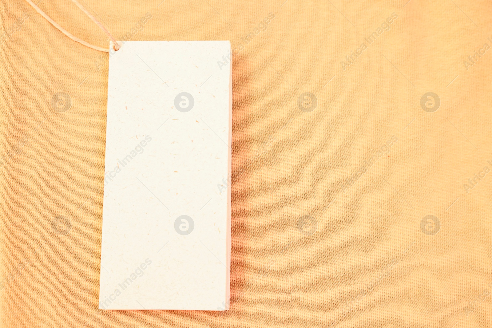 Photo of Cardboard tag on beige garment, top view. Space for text