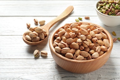 Photo of Organic pistachio nuts in bowl and spoon on wooden table, space for text