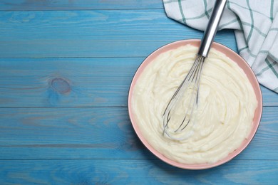 Photo of Pastry cream with balloon whisk on light blue wooden table, flat lay. Space for text