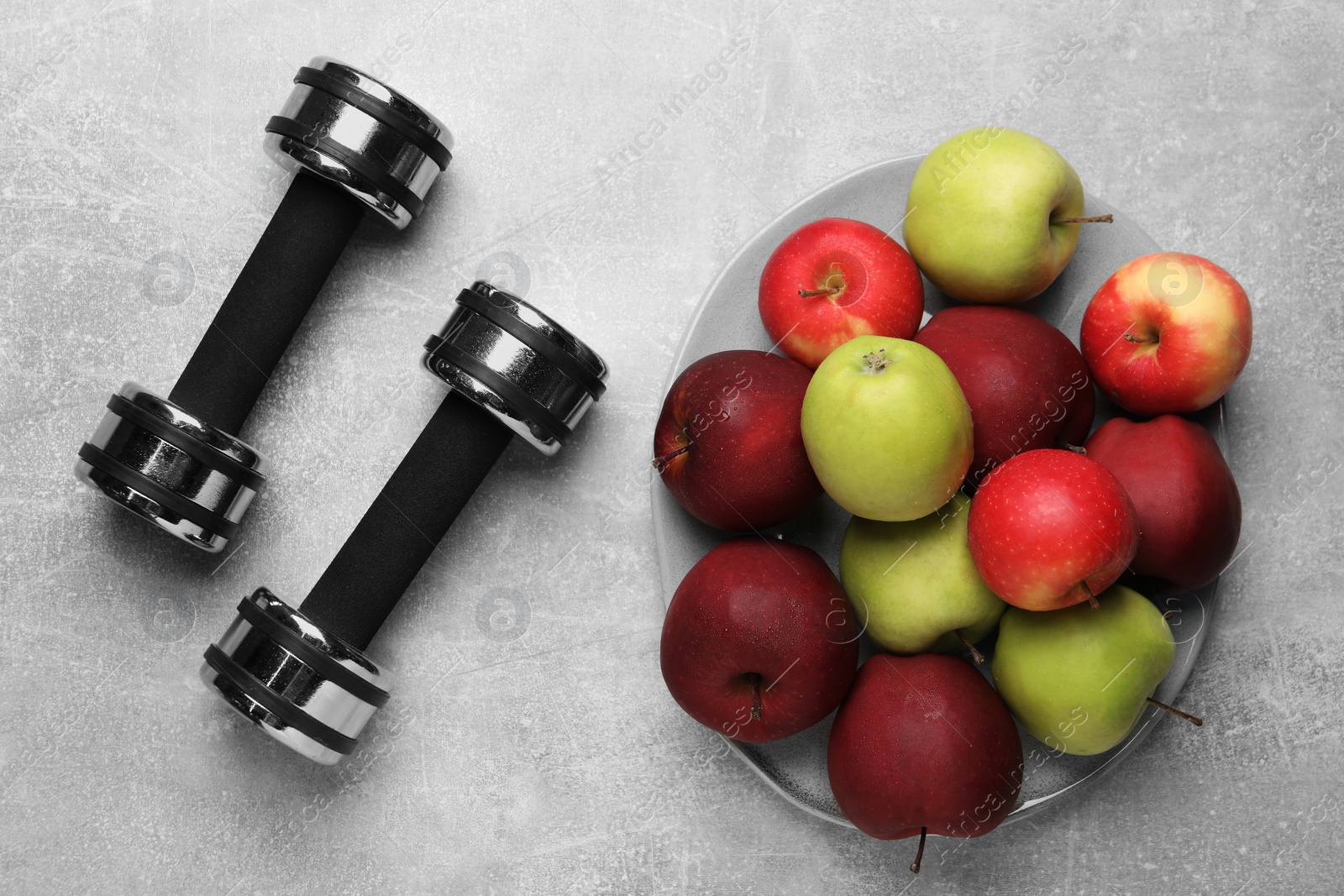 Photo of Healthy diet. Plate with apples and dumbbells on light grey textured table, flat lay