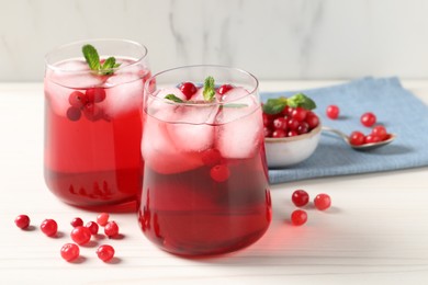 Photo of Tasty cranberry juice with ice cubes in glasses and fresh berries on white wooden table, closeup