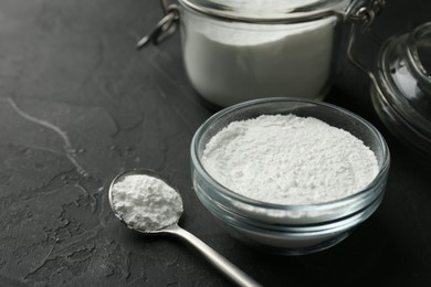 Photo of Baking powder in bowl, jar and spoon on black textured table, closeup. Space for text