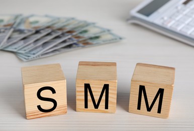 Photo of Cubes with abbreviation SMM (Social media marketing), money and calculator on white wooden table