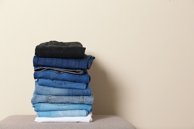 Photo of Stack of different jeans on ottoman against light background. Space for text