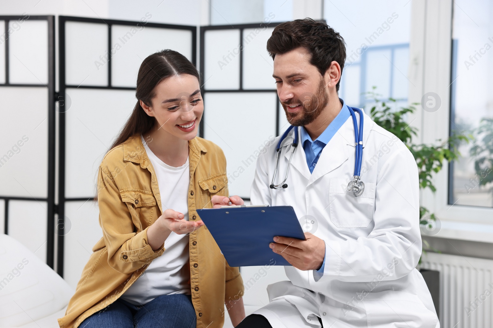 Photo of Doctor with clipboard consulting patient during appointment in clinic