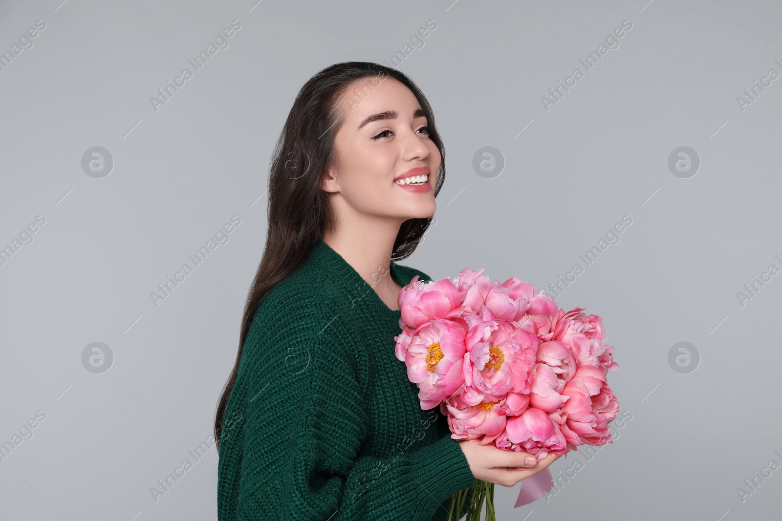 Photo of Beautiful young woman with bouquet of peonies on light grey background