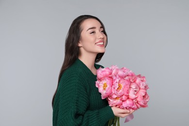 Beautiful young woman with bouquet of peonies on light grey background
