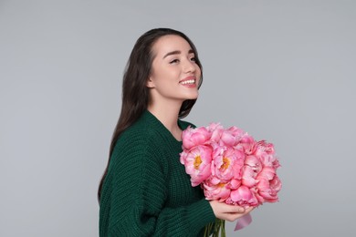 Photo of Beautiful young woman with bouquet of peonies on light grey background