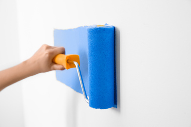 Photo of Woman painting white wall with blue dye, closeup. Interior renovation