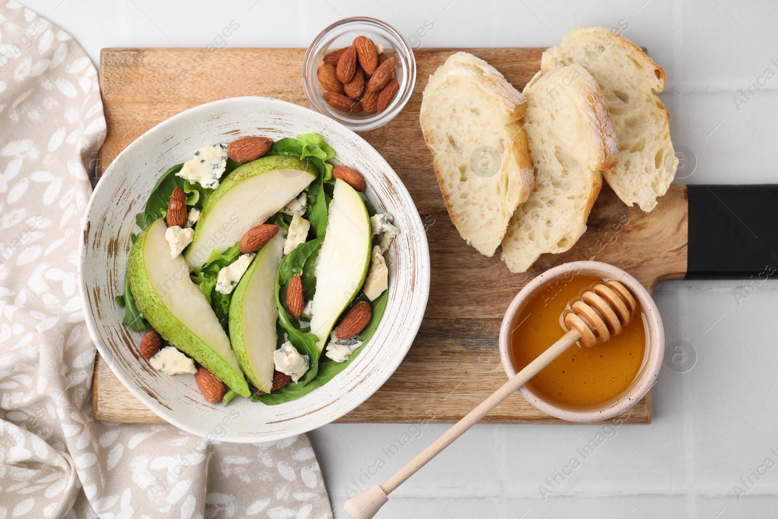 Photo of Delicious pear salad in bowl, honey and bread on light tiled table, top view