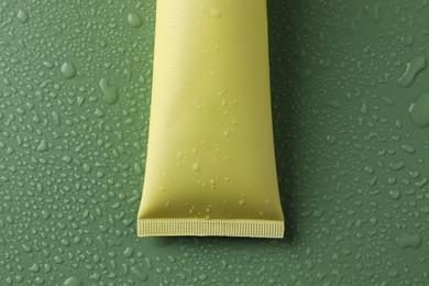 Photo of Moisturizing cream in tube on green background with water drops, top view