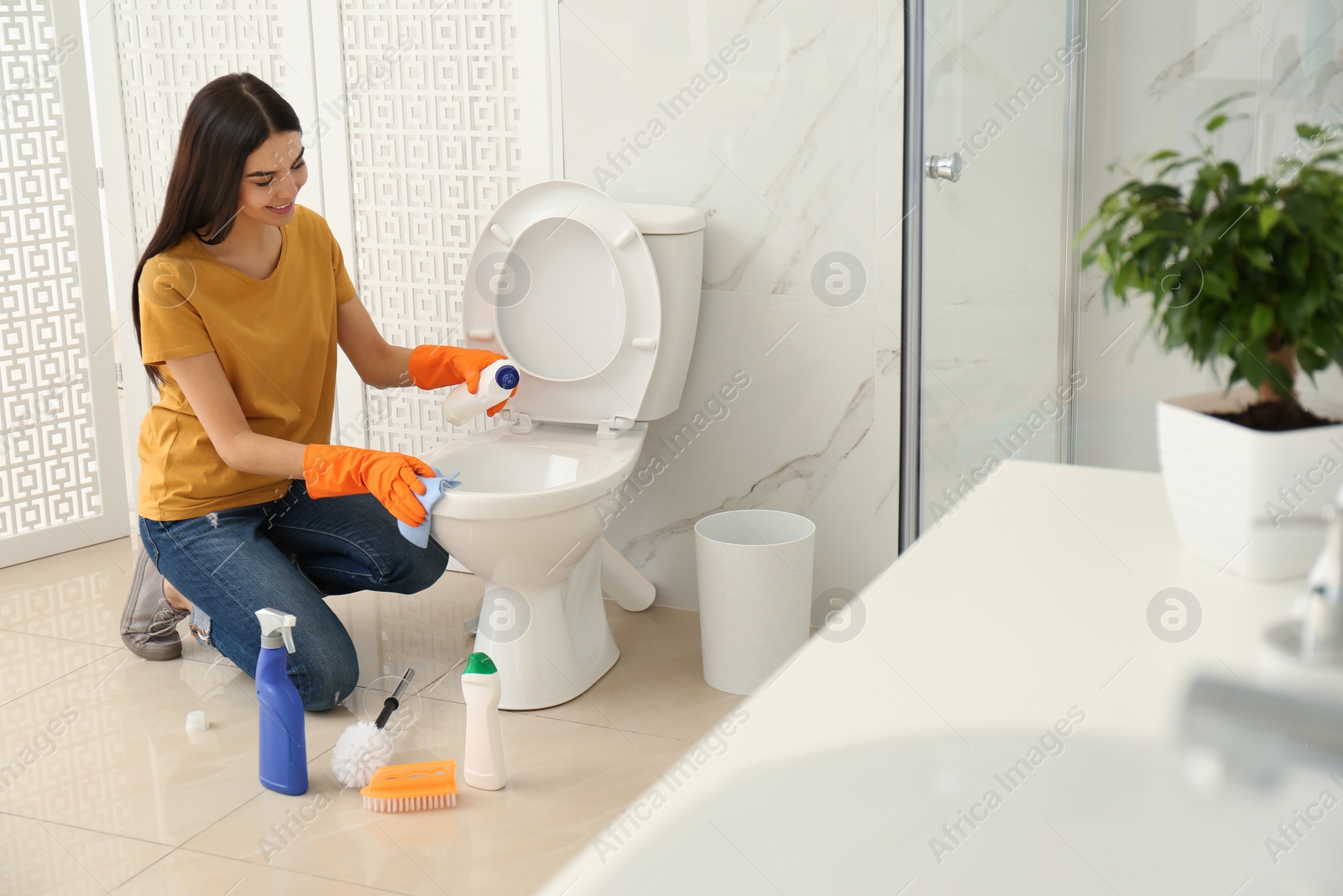 Photo of Young woman cleaning toilet bowl in bathroom