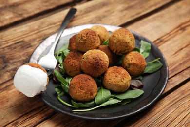 Delicious falafel balls with spinach and sauce on wooden table, closeup