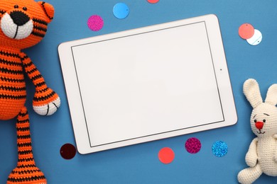 Modern tablet, confetti and stuffed animals on blue background, flat lay. Space for text