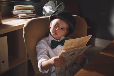 Photo of Cute little detective with newspaper in office