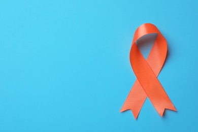 Orange ribbon on light blue background, top view with space for text. Multiple sclerosis awareness