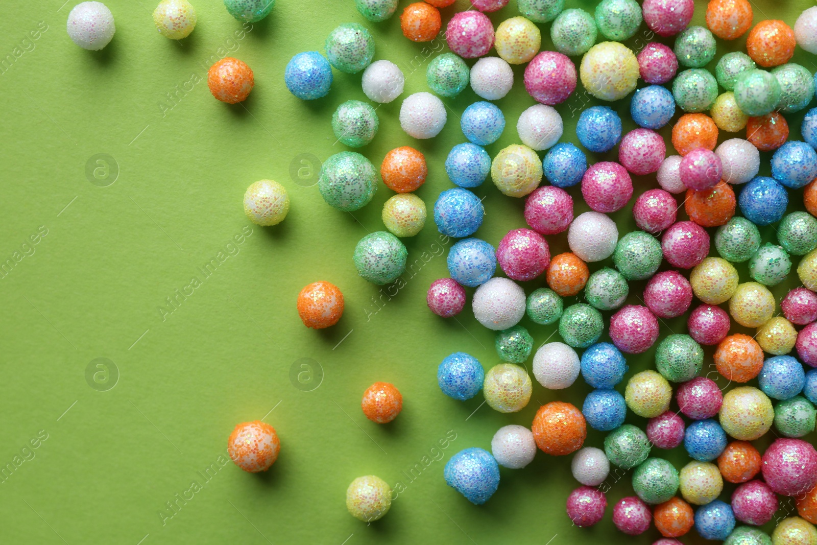 Photo of Small colorful beads on green background, flat lay
