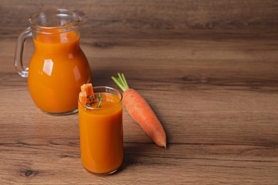 Photo of Carrot juice in glass and jug on wooden table