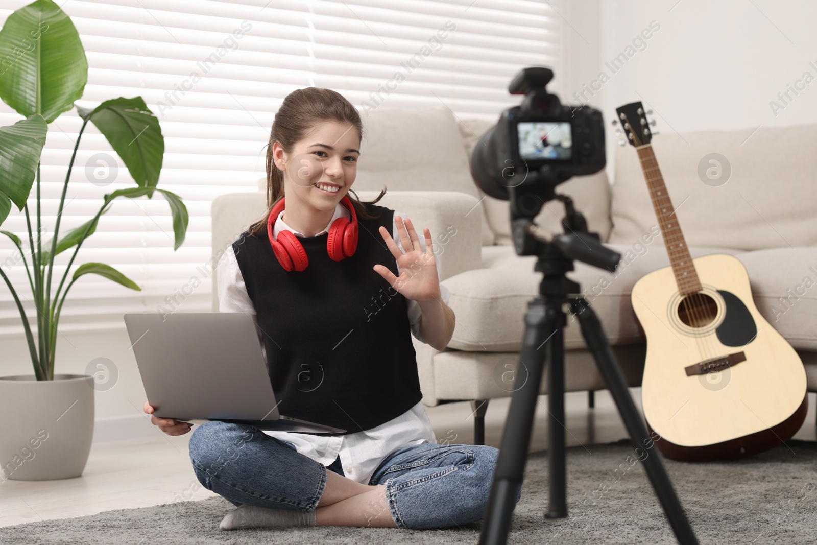 Photo of Smiling teenage blogger with laptop waving hello to her subscribers while streaming at home