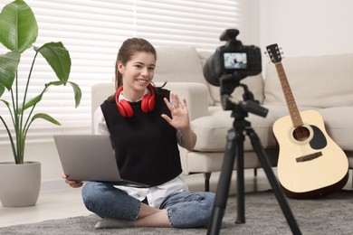 Smiling teenage blogger with laptop waving hello to her subscribers while streaming at home