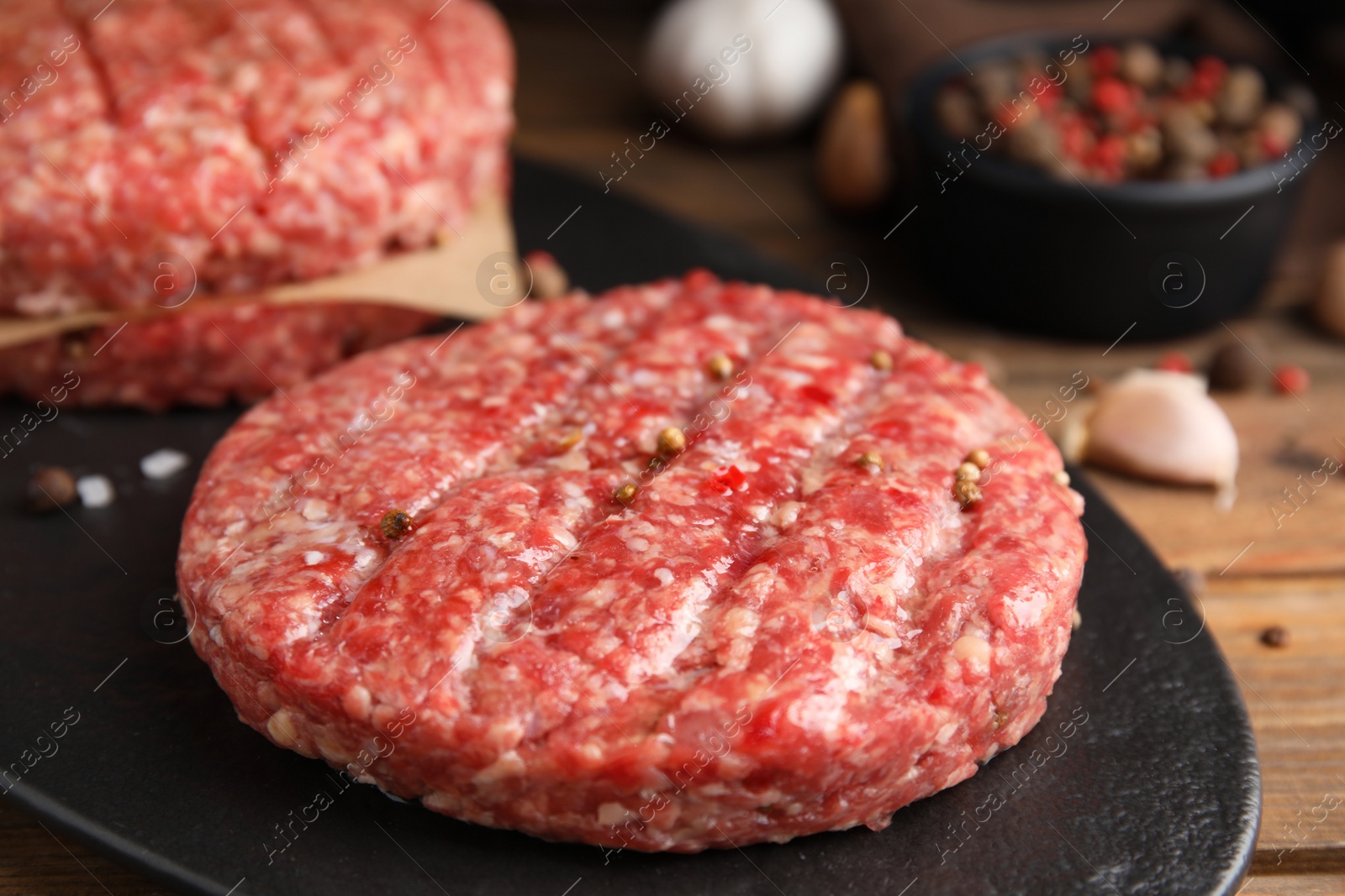 Photo of Raw hamburger patties with pepper on black board, closeup