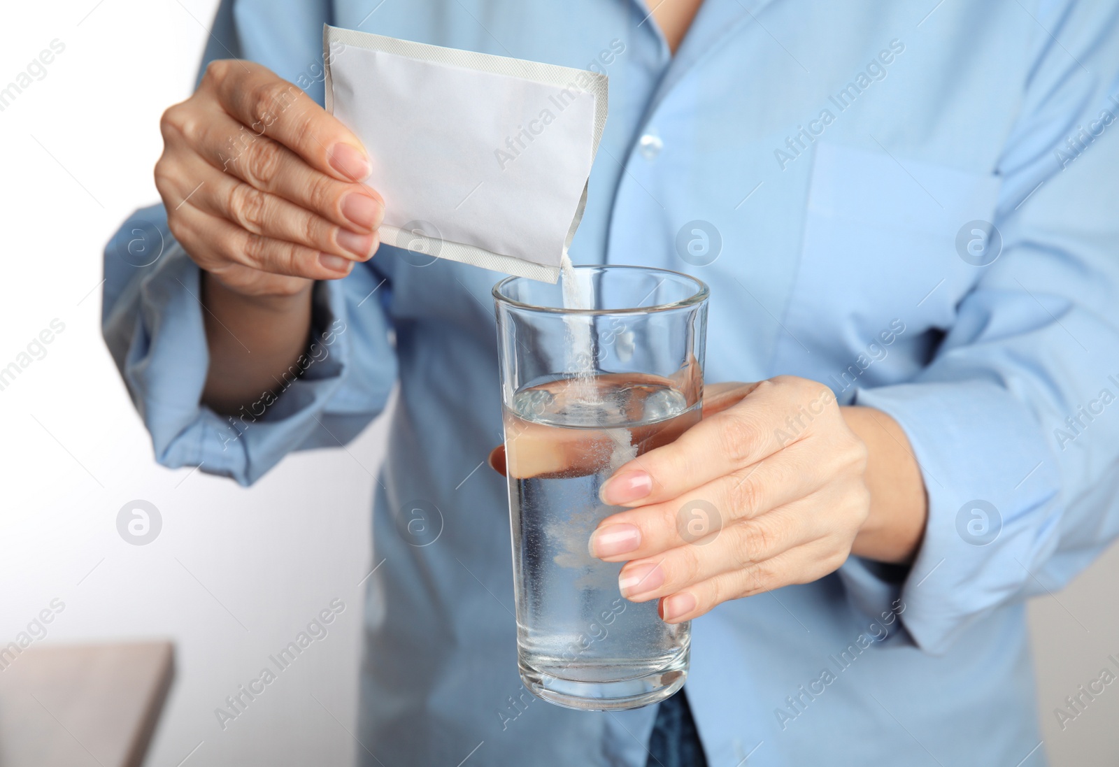 Photo of Woman pouring powder from medicine sachet into glass with water, closeup