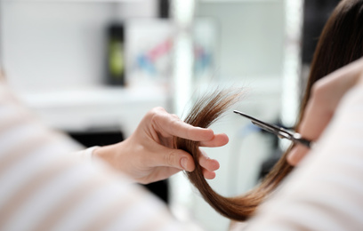 Hairdresser making stylish haircut with professional scissors in salon, closeup